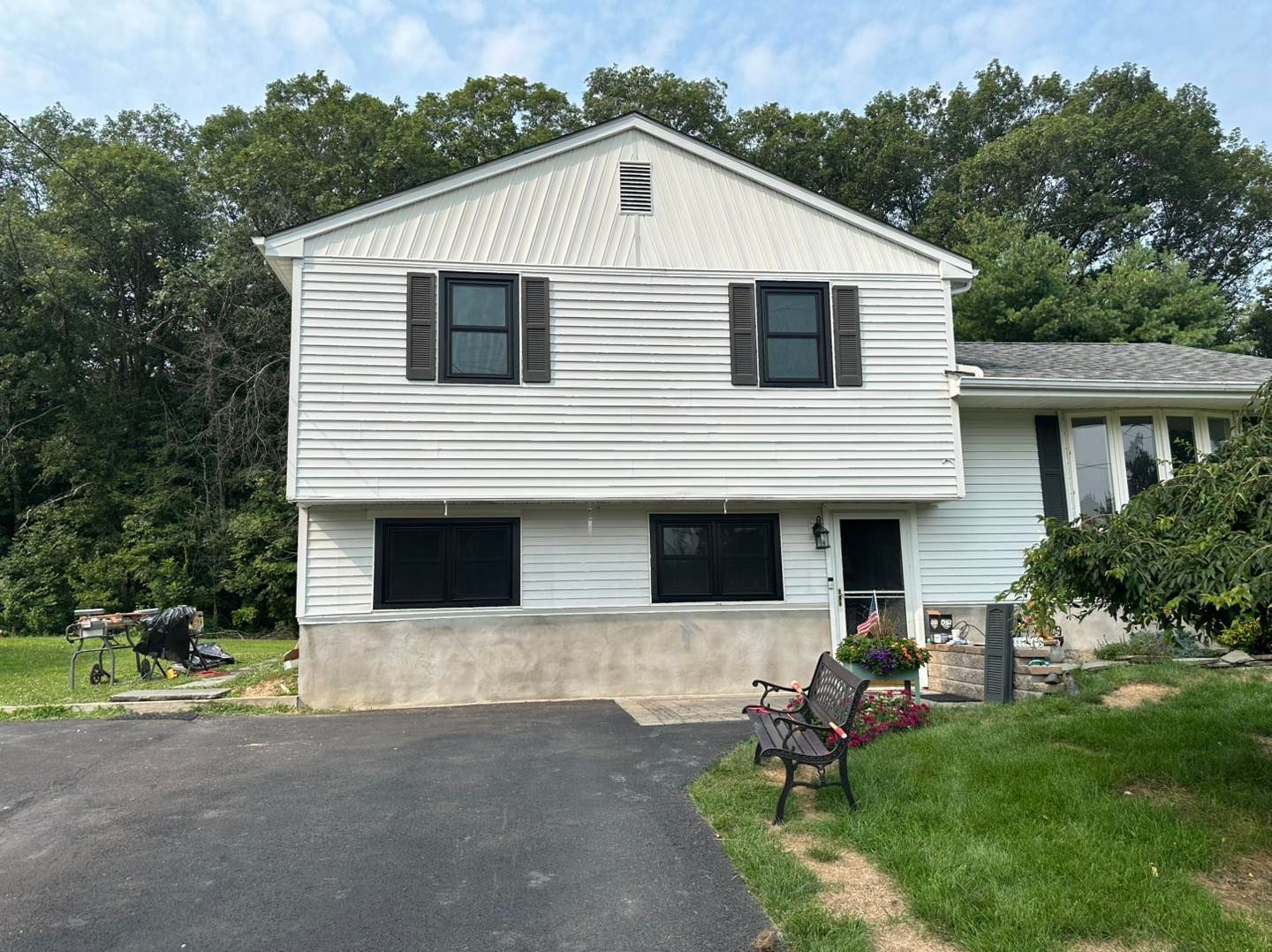 Two-story white house with dark window shutters, surrounded by trees and a driveway.