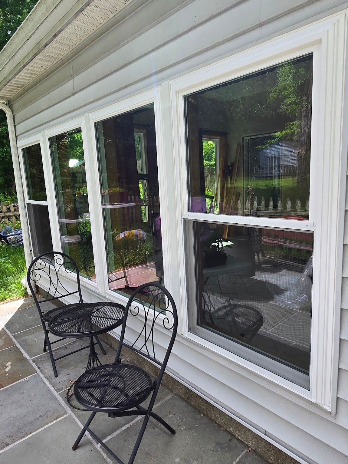 Black wrought iron patio set next to windows on a gray building. Windows reflect outdoor scene.