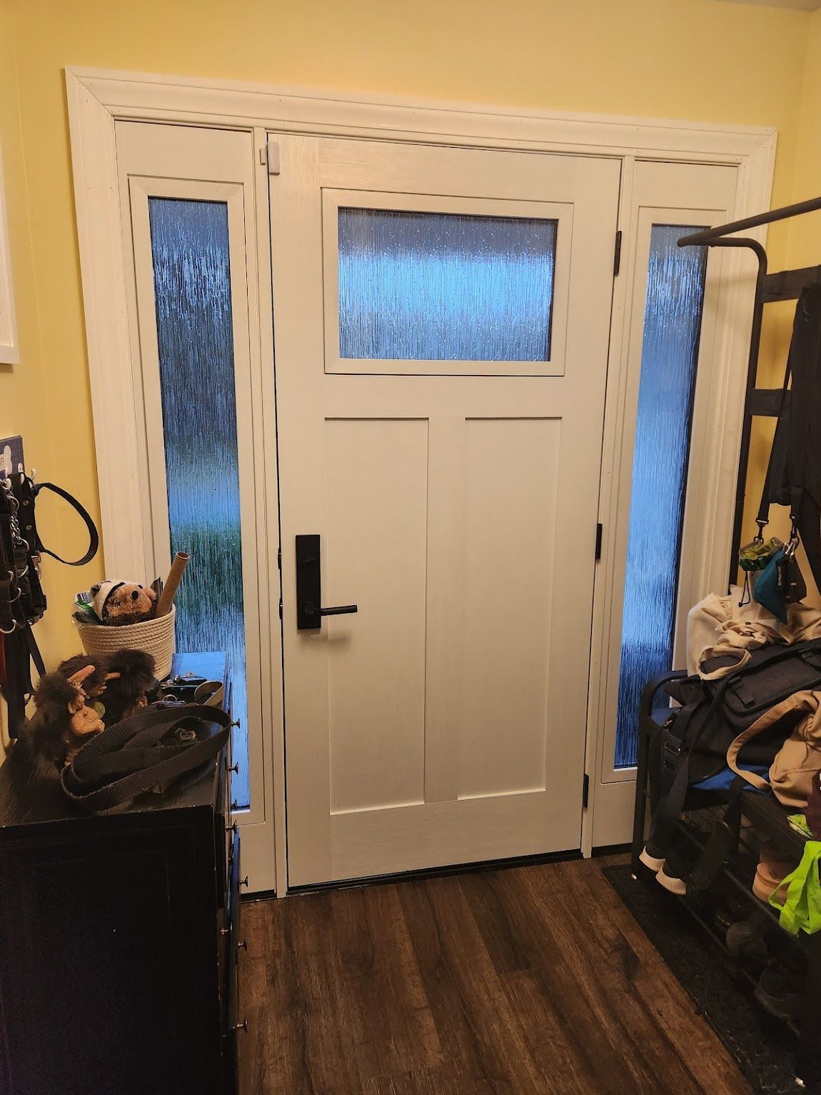 White front door with sidelights, black handle, and textured glass, indoor setting.