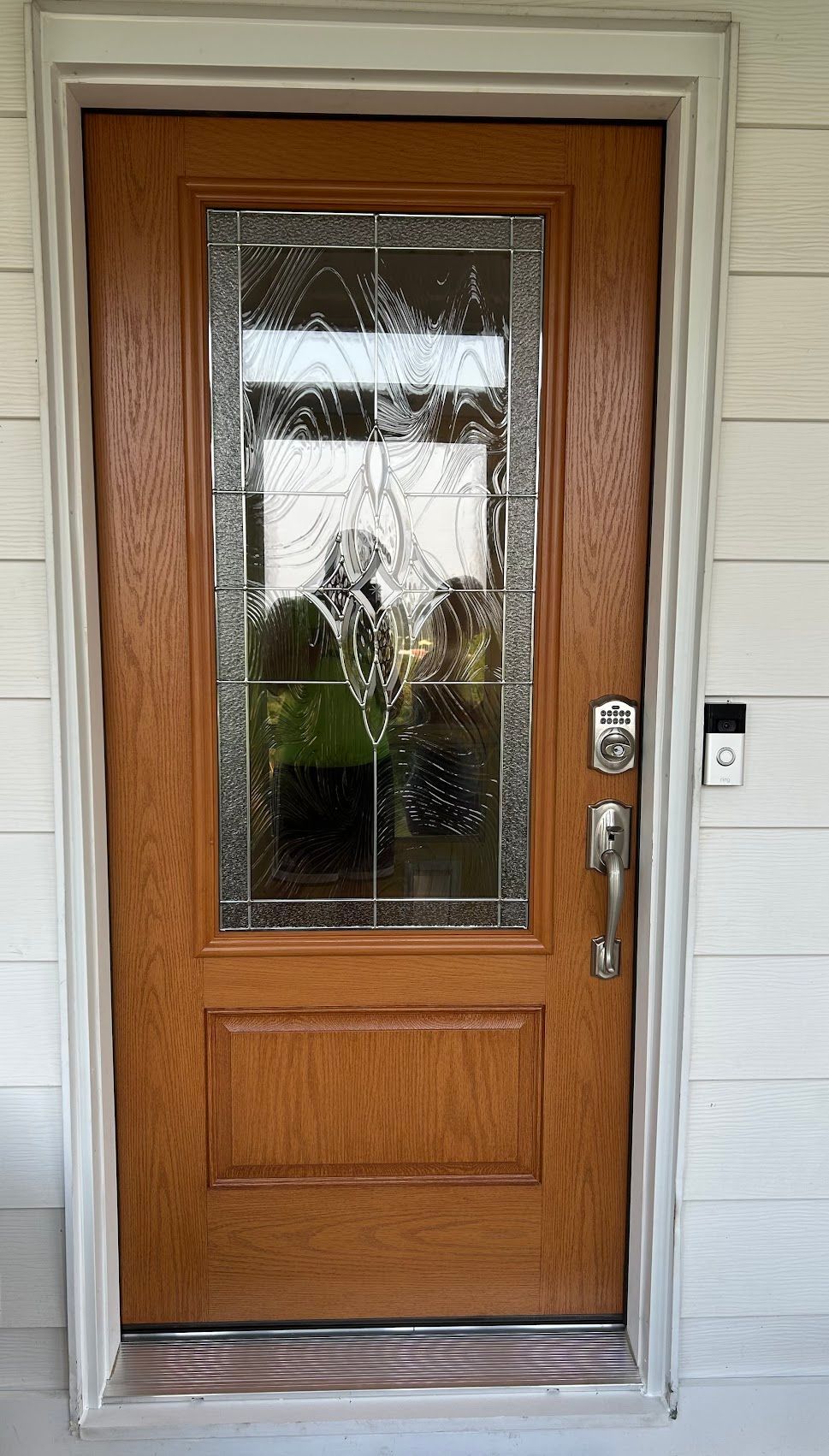 Wooden front door with glass panel, silver hardware, and Ring doorbell on white siding.