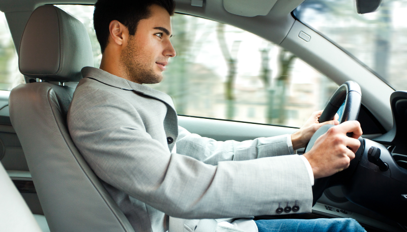 Young professional male wearing a work blazer in the front seat of a car driving fast.