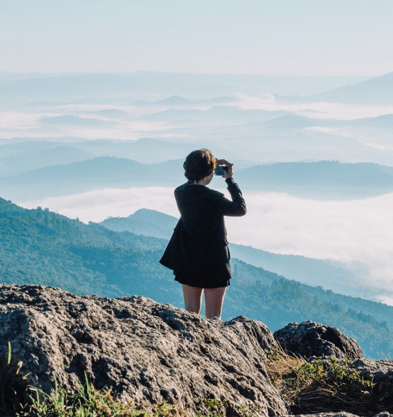 business woman on top of mountain searching the horizon