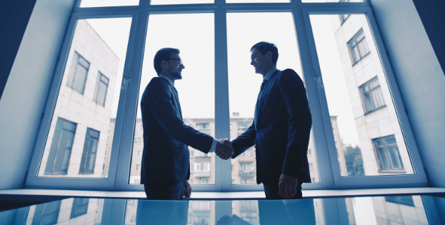 Silhouette of two business men shaking hands after a meeting in a corporate building.