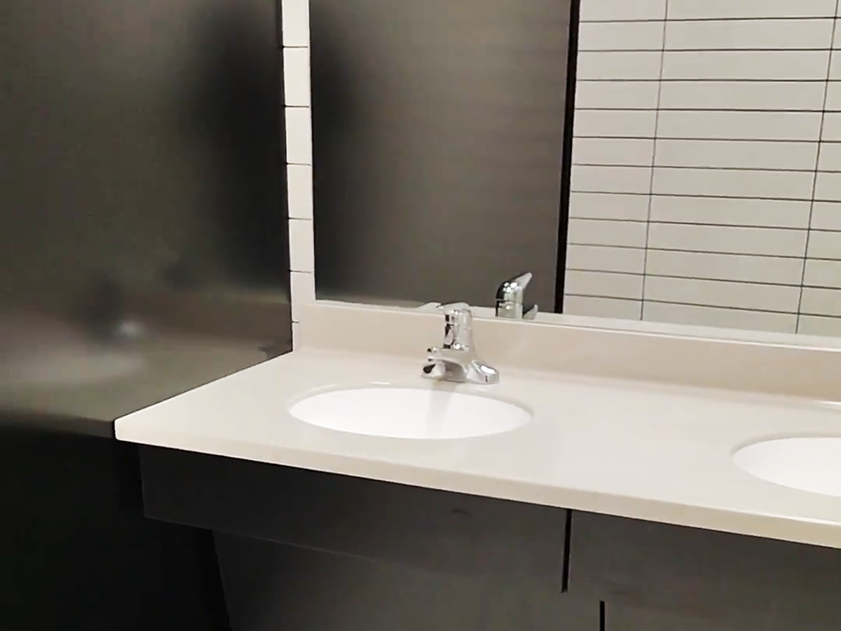 Bathroom sink with white countertop, chrome faucet, and rectangular mirror. Grey cabinetry below.