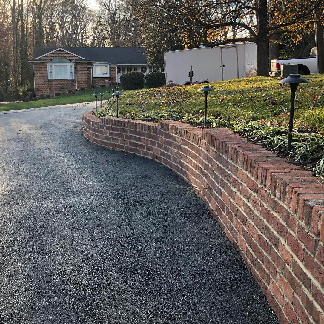 A brick wall along the side of a driveway next to a house.