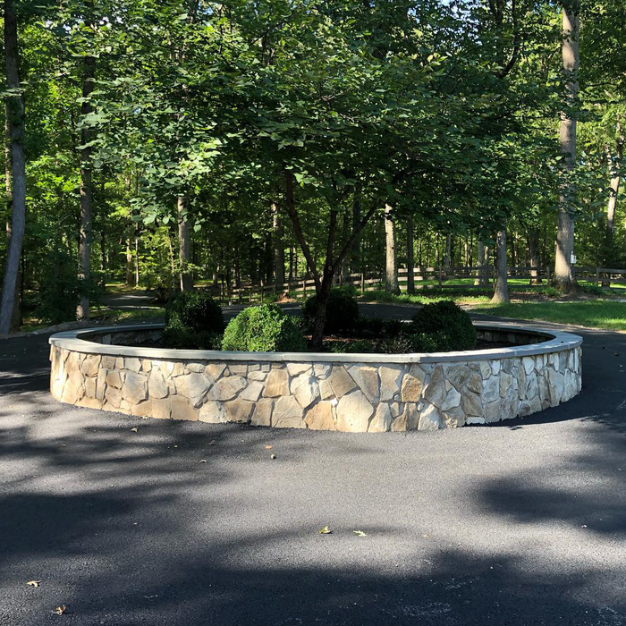 A stone wall in the middle of a driveway with trees in the background.