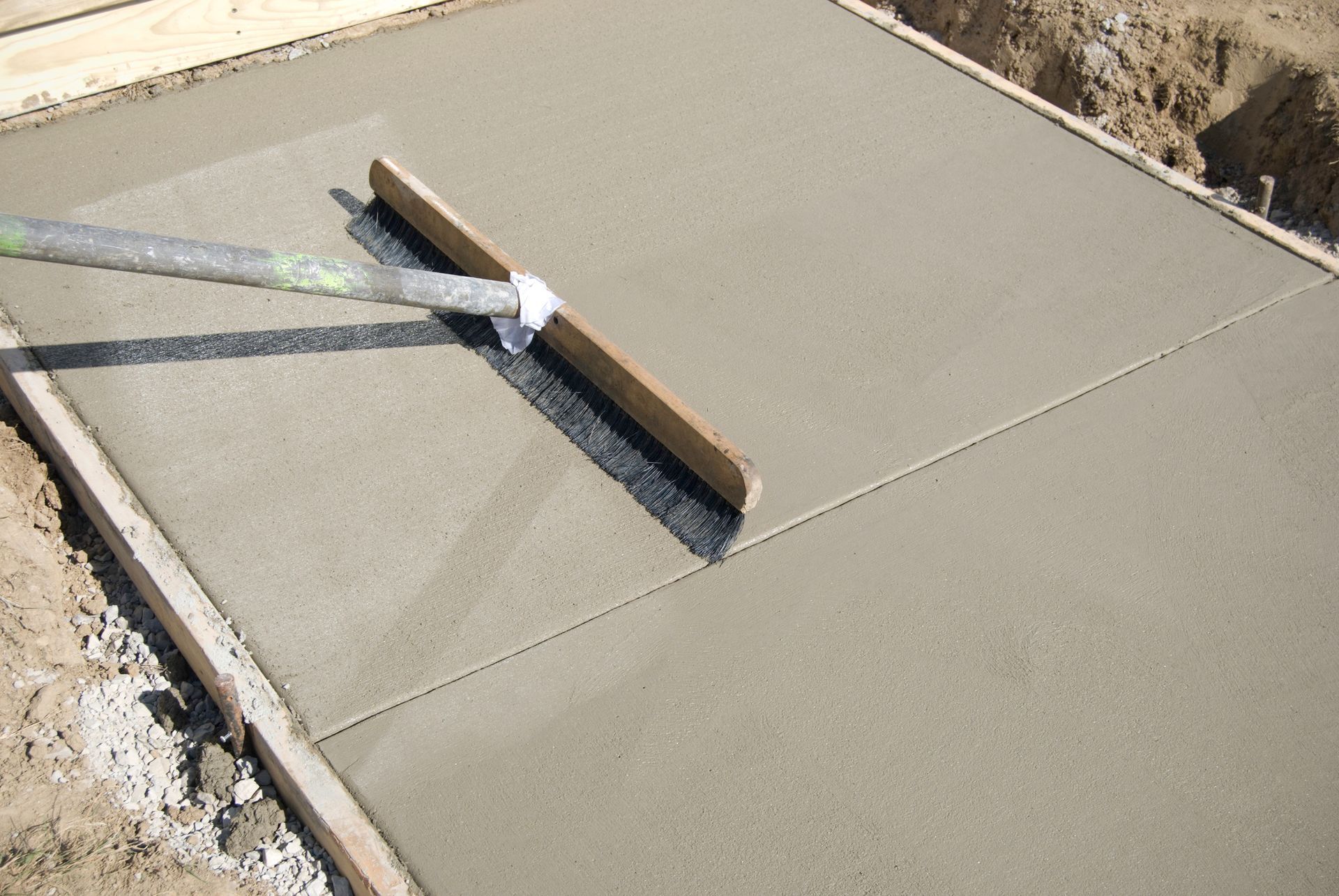 A person levels wet concrete in a wooden frame with a long-handled screed.