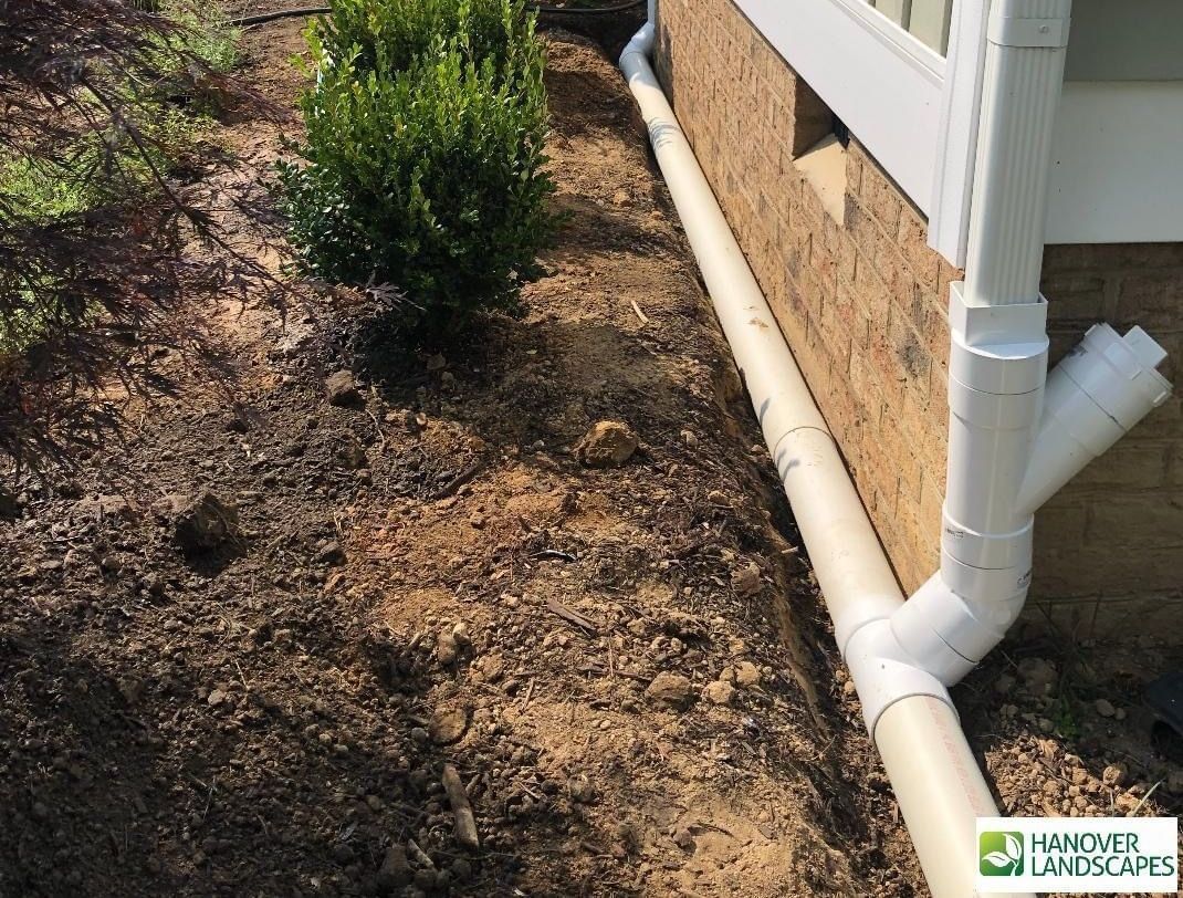Beige drainage pipe installed along a brick wall under a white gutter.