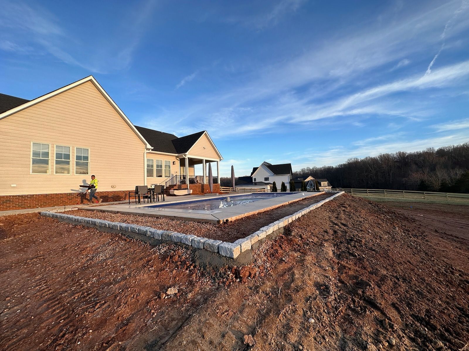 Backyard with house and patio construction; brick retaining wall, dirt ground, blue sky.