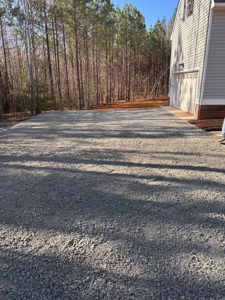 Gravel driveway next to a light-colored house. Trees in the background under a blue sky.