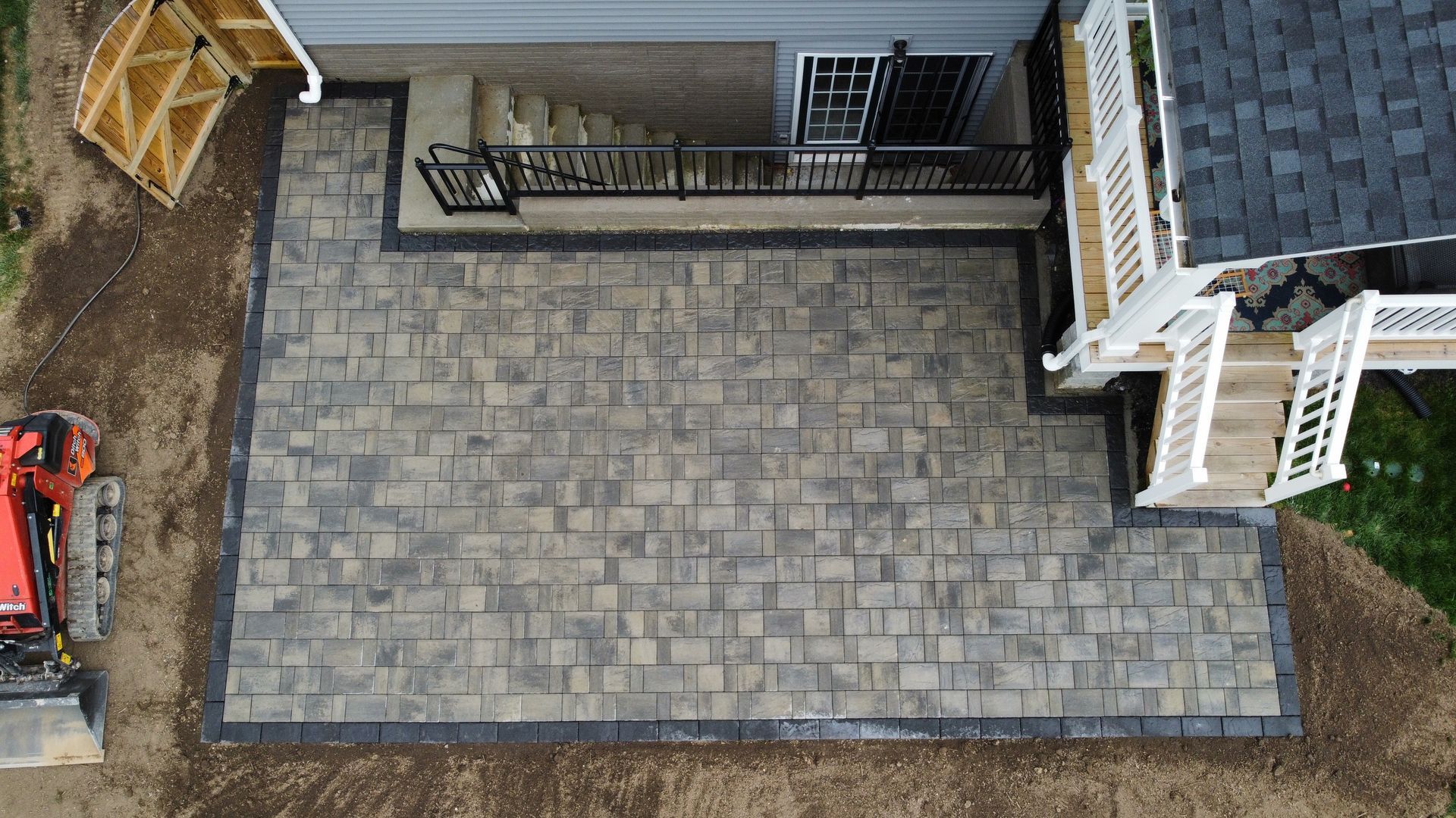 Overhead view of a finished brick patio adjacent to a house with steps. Dark border around the patio.