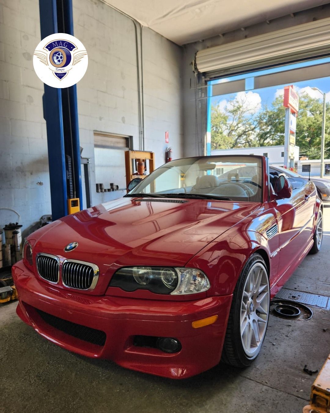 Red BMW coupe in an auto shop bay, facing forward near a lift.