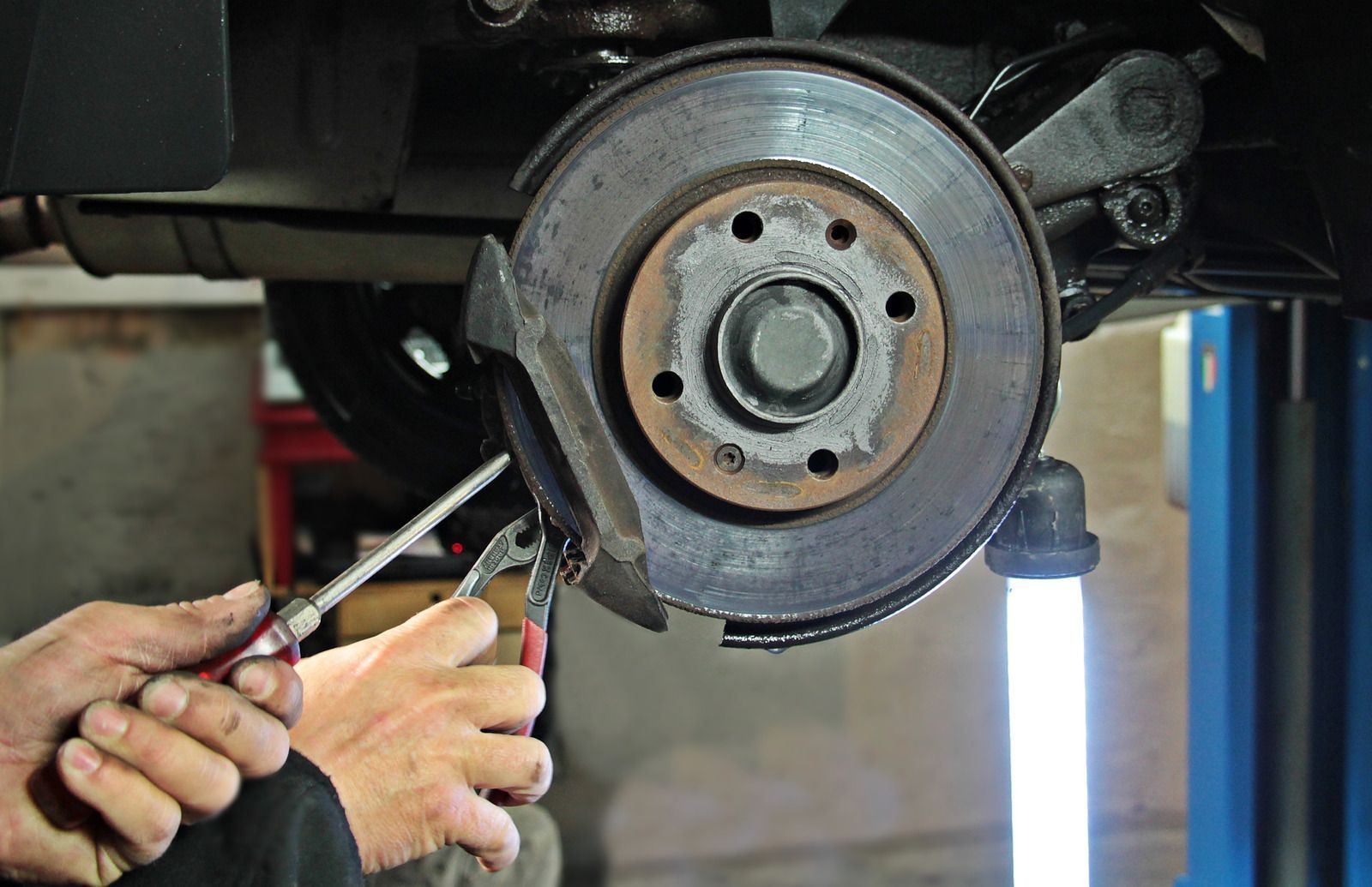Mechanic using pliers to work on a car’s exposed brake assembly on a lift