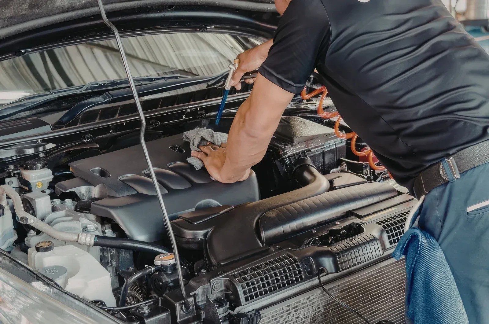 Mechanic working under an open car hood in a garage