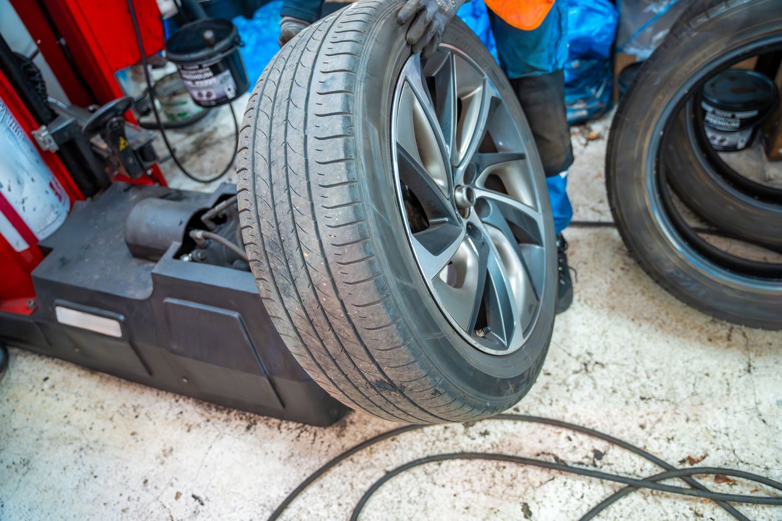 Car tire mounted on a wheel balancer in an auto repair shop, with tools and cables nearby