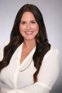 A woman with long dark hair is wearing a white shirt and smiling.