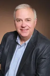 A man in a suit and blue shirt is smiling for the camera.