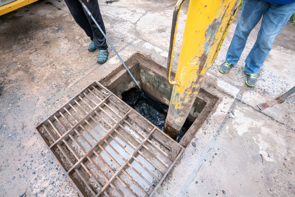 A Manhole Cover Is Being Opened By A Yellow Excavator — Barney Hinds Plumbing In Point Vernon, QLD