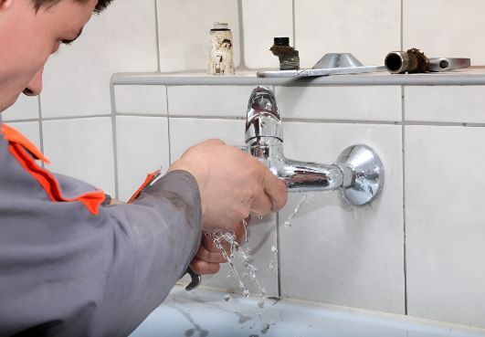 A Man Is Fixing A Faucet In A Bathroom — Barney Hinds Plumbing In Point Vernon, QLD