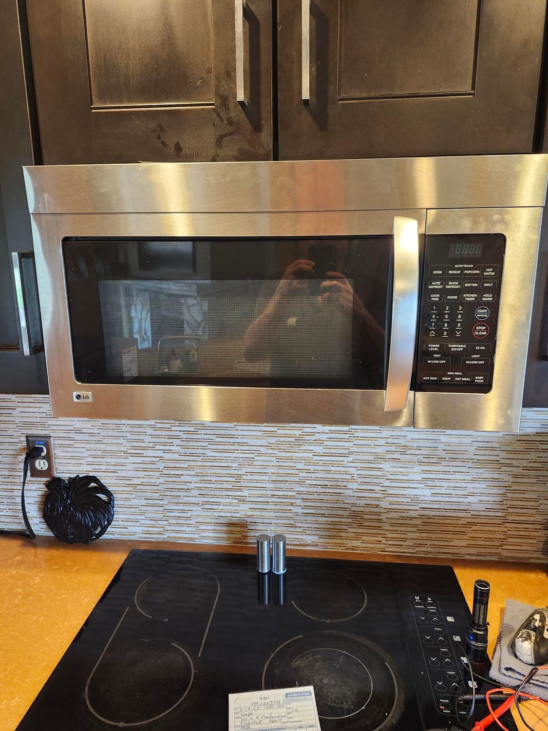 Stainless steel microwave above a black cooktop in a kitchen.