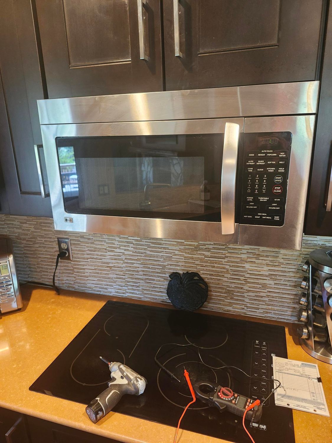 Microwave over a black cooktop, with tools on the counter.