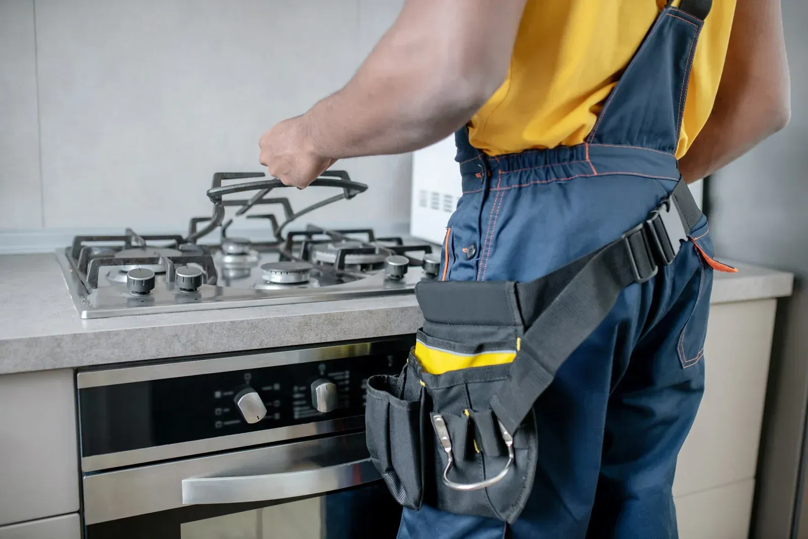 A man is fixing a gas stove in a kitchen.