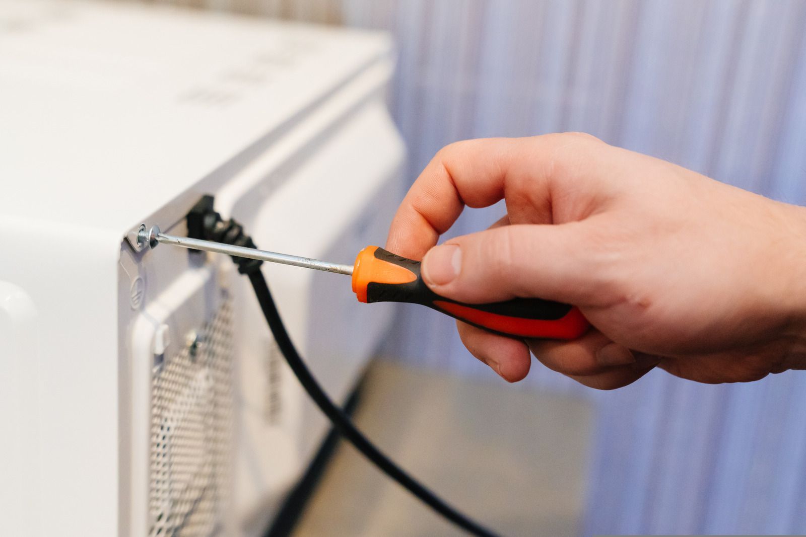 A person is fixing a microwave with a screwdriver.