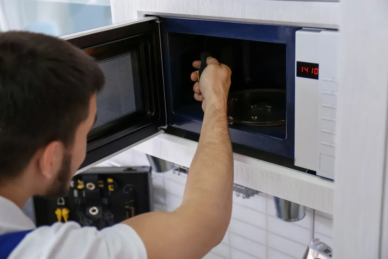 A man is fixing a microwave in a kitchen.