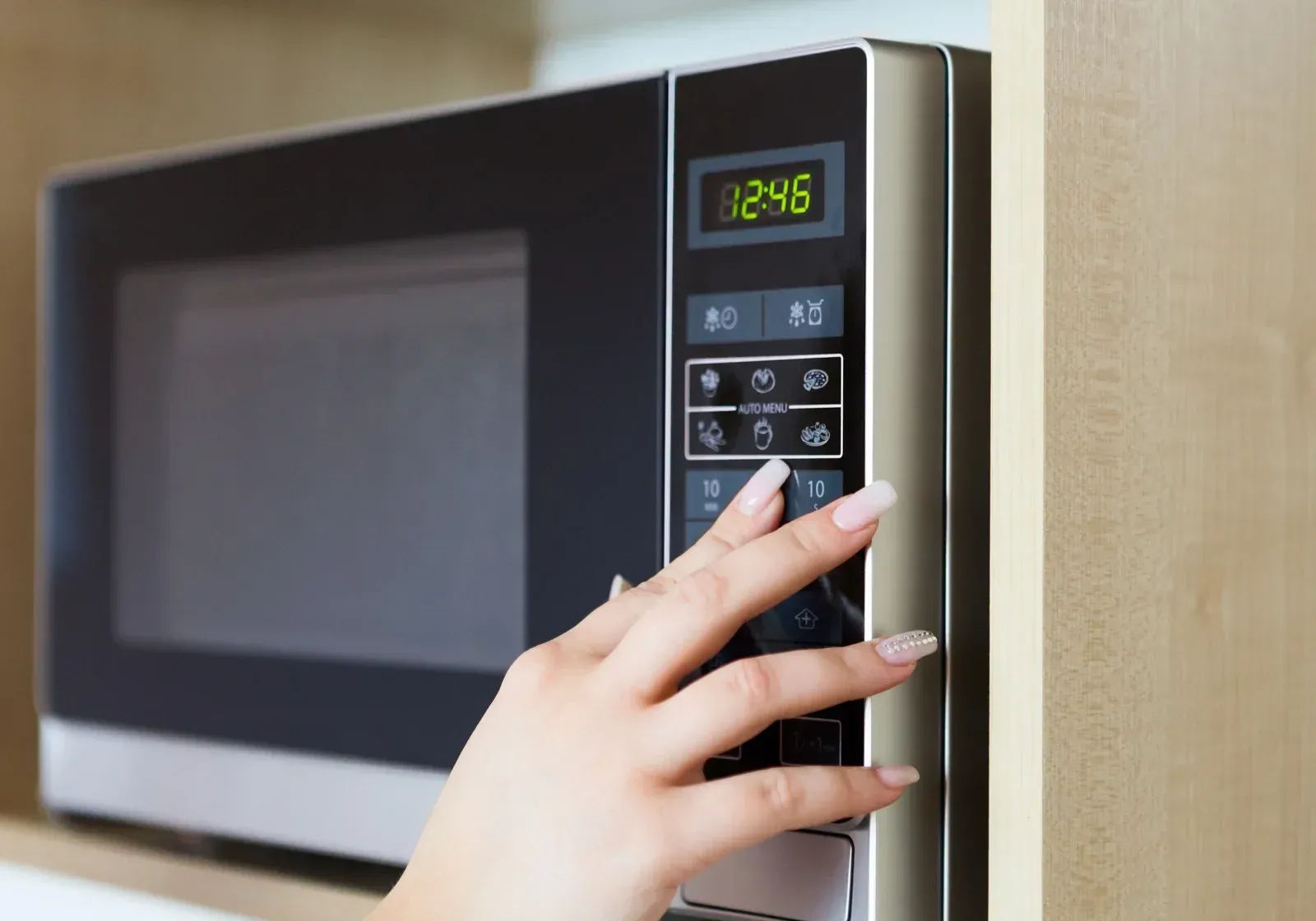 A woman 's hand is pressing a button on a microwave.