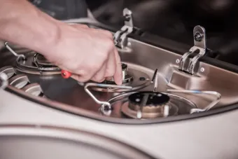 A person is fixing a stove with a screwdriver.