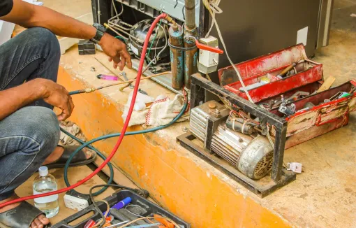 A man is working on a refrigerator with a hose.