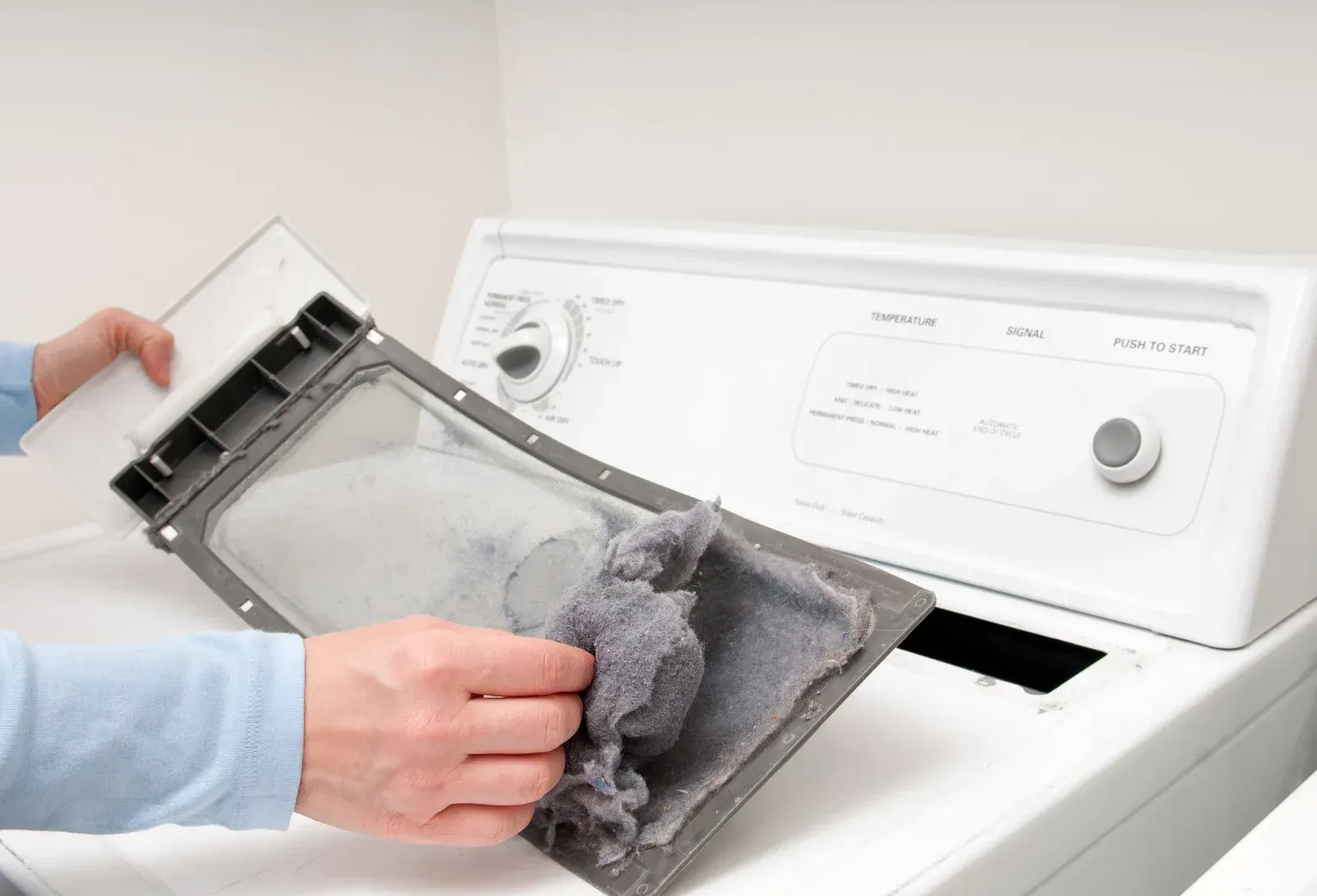A person is cleaning a dryer filter with a cloth.