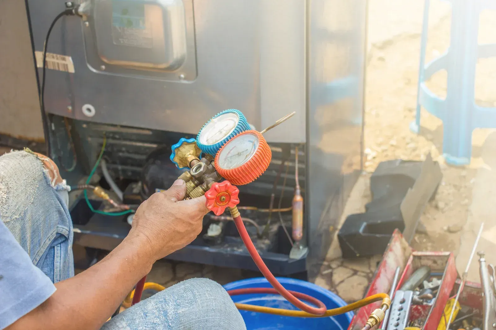 A man is fixing a refrigerator with a gauge.