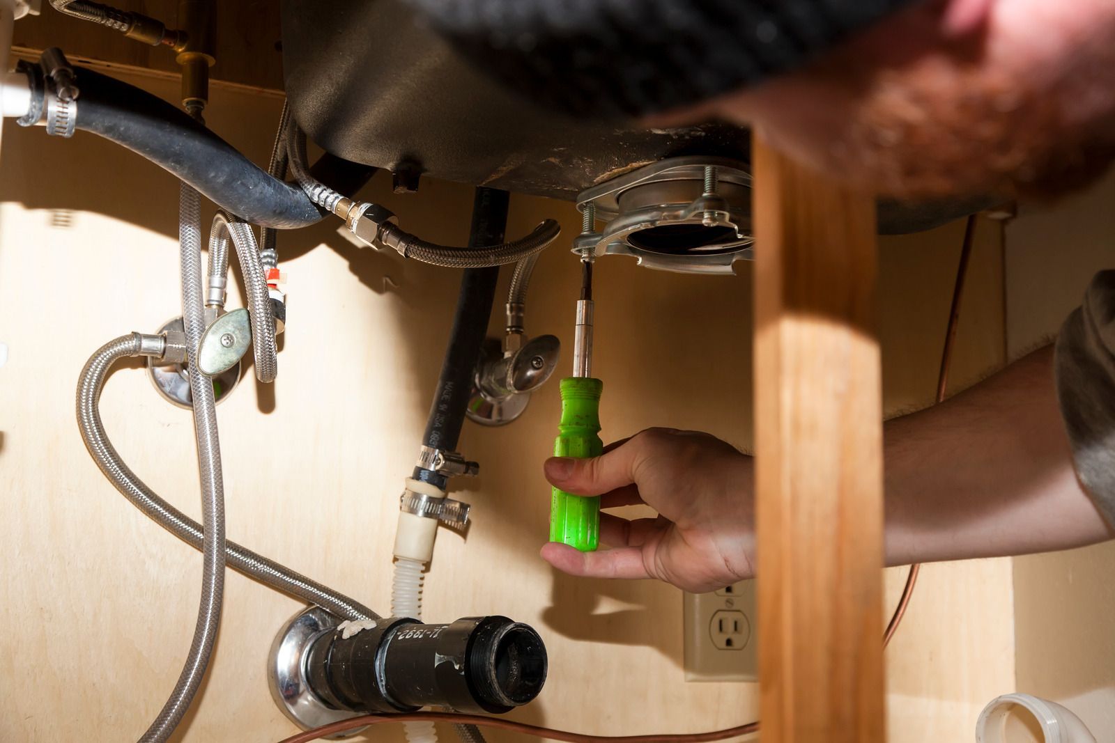 A man is fixing a sink with a green screwdriver.