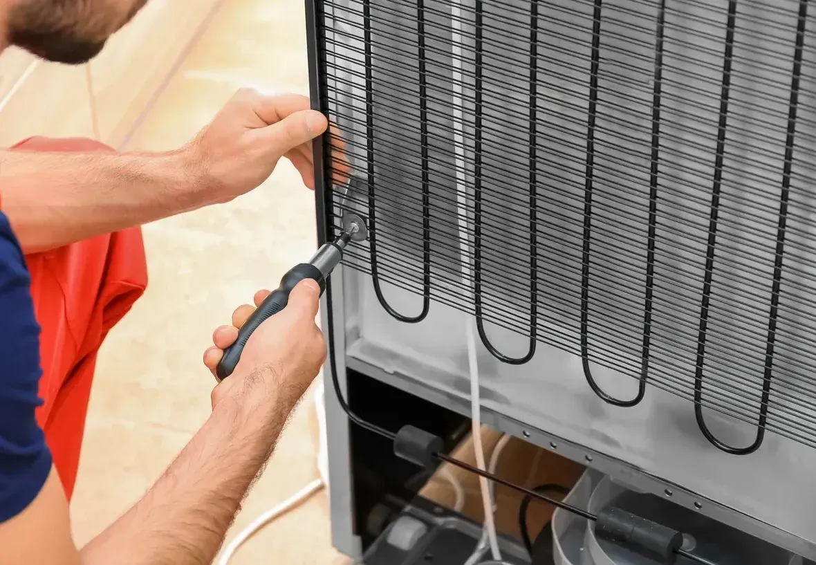 A man is fixing a refrigerator with a screwdriver.