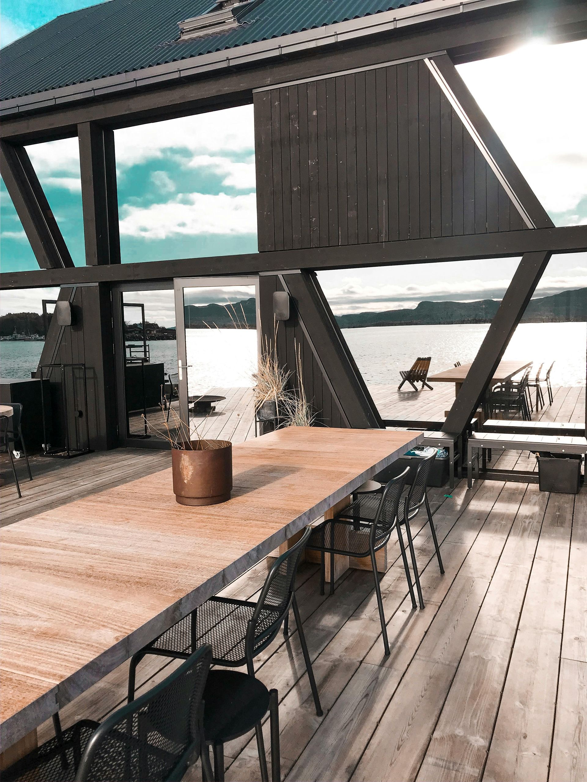A large wooden table and chairs on a deck overlooking a body of water