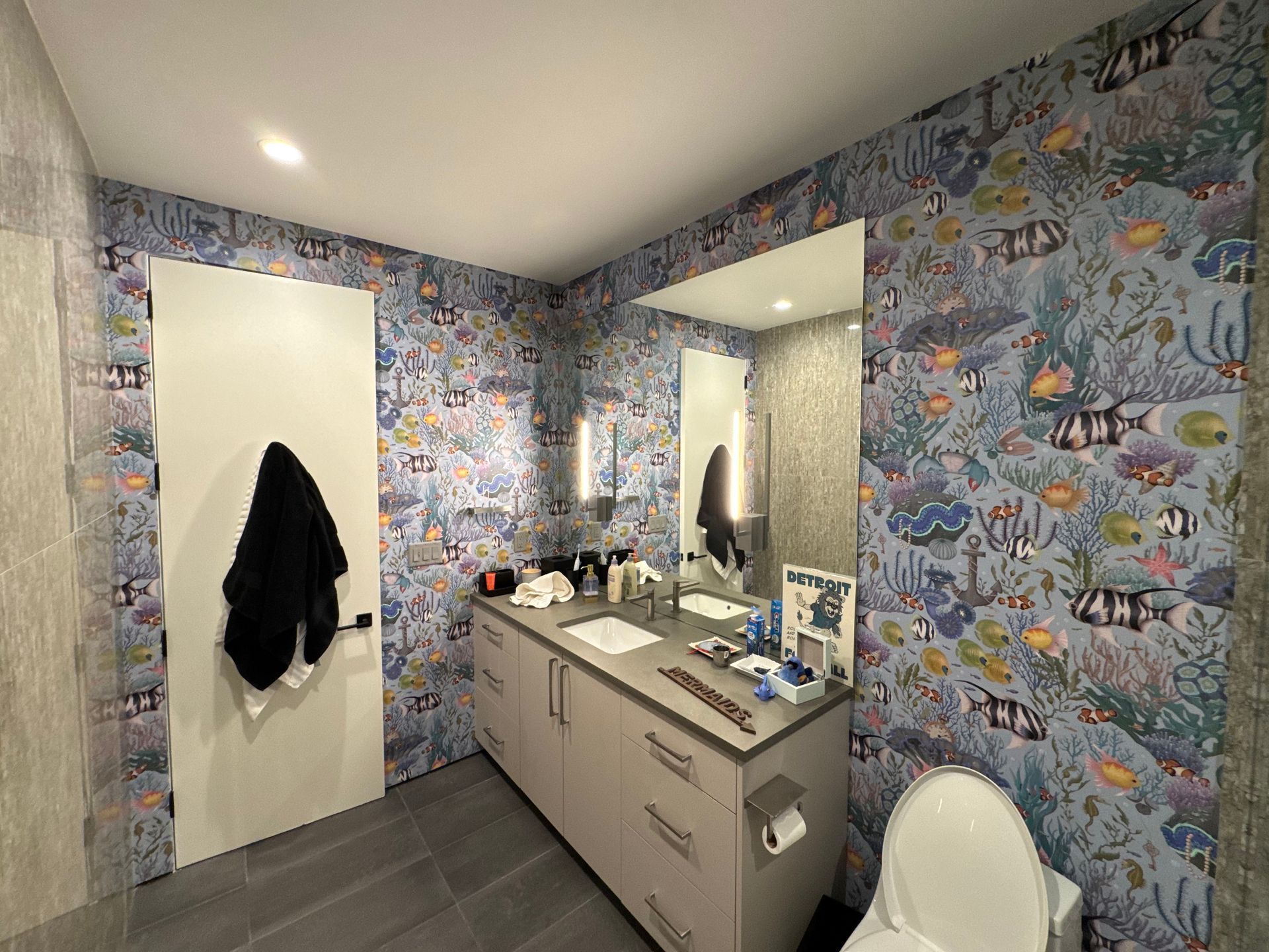 A bathroom with a toilet , sink , mirror and wallpaper.