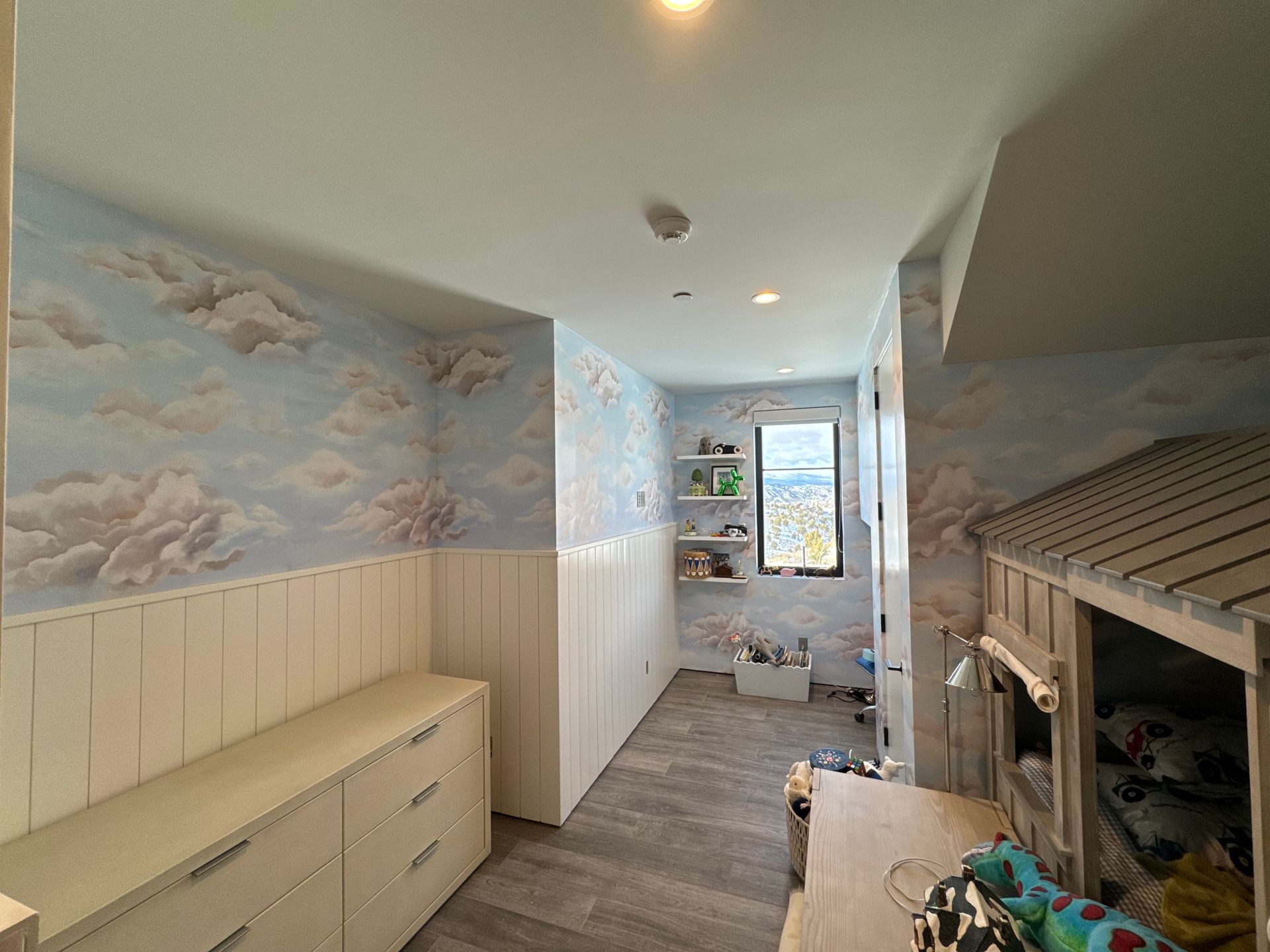 A child 's room with a bunk bed , dressers , shelves and a window.