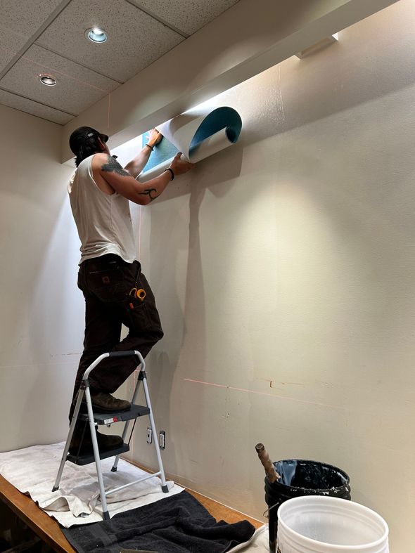 A man is standing on a ladder applying wallpaper to a wall.