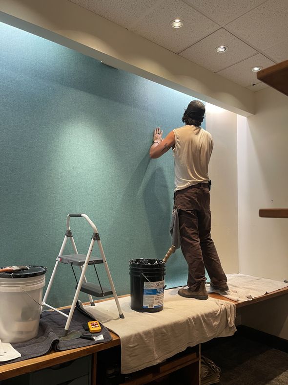 A man is standing on a table painting a wall.
