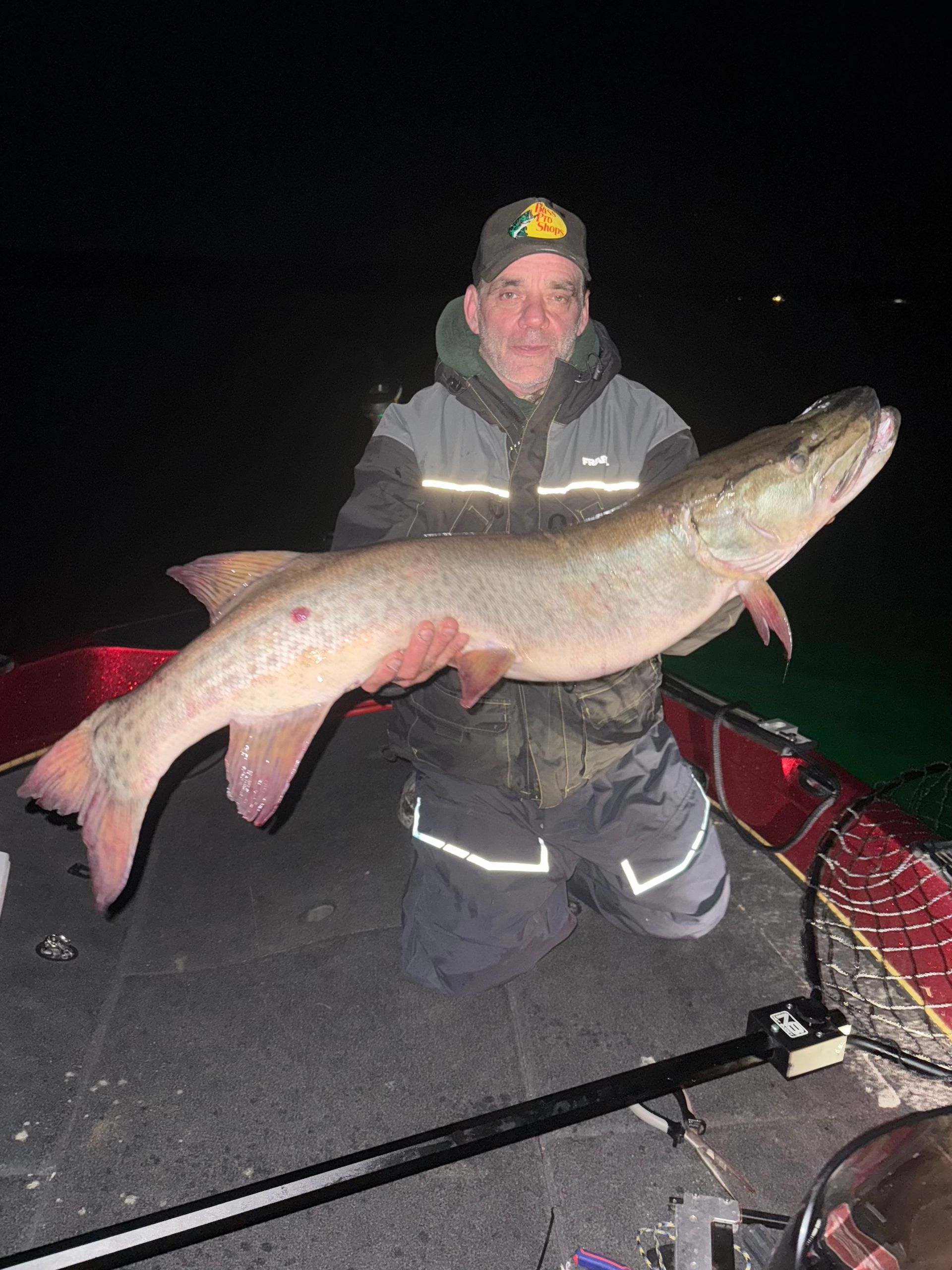 Dan Freund holding a large muskie fish on a boat at night.