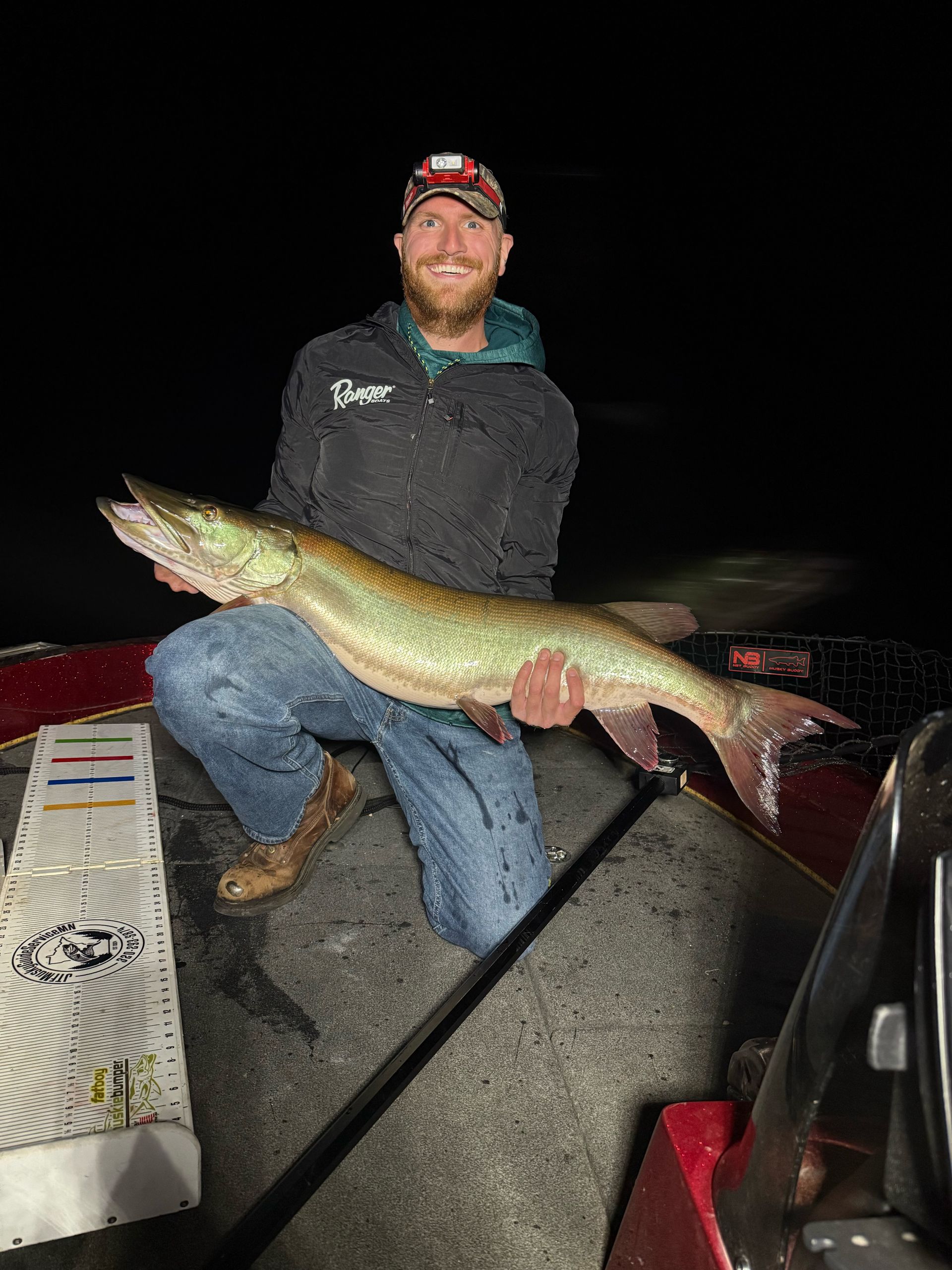 Man kneeling in boat holding a large fish, at night.