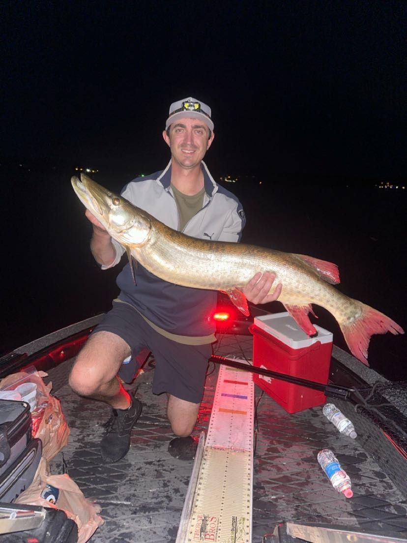 Man kneeling in boat holds large fish at night.