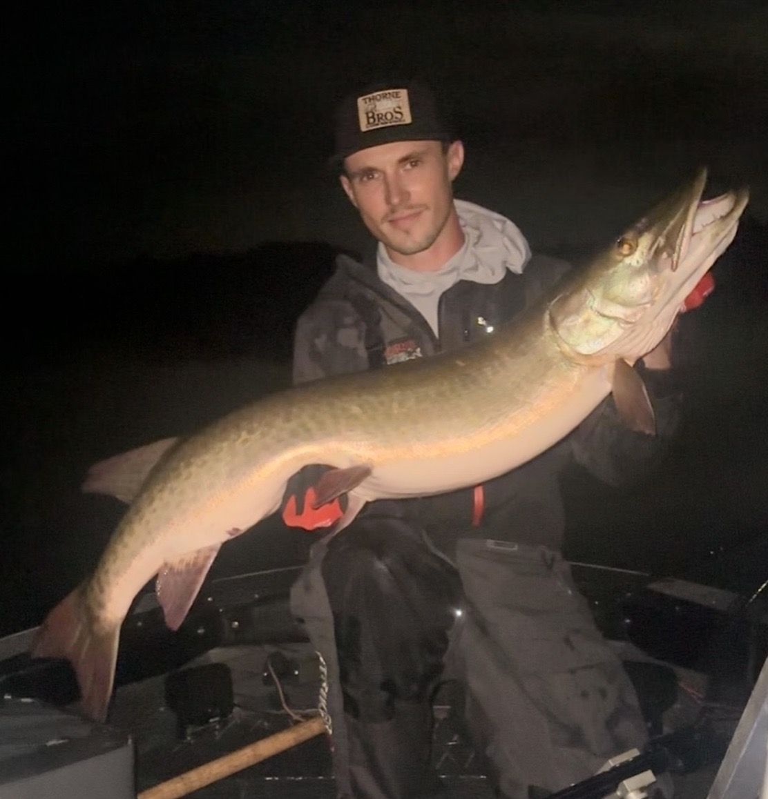 Man holding a large muskie fish in a boat at night.