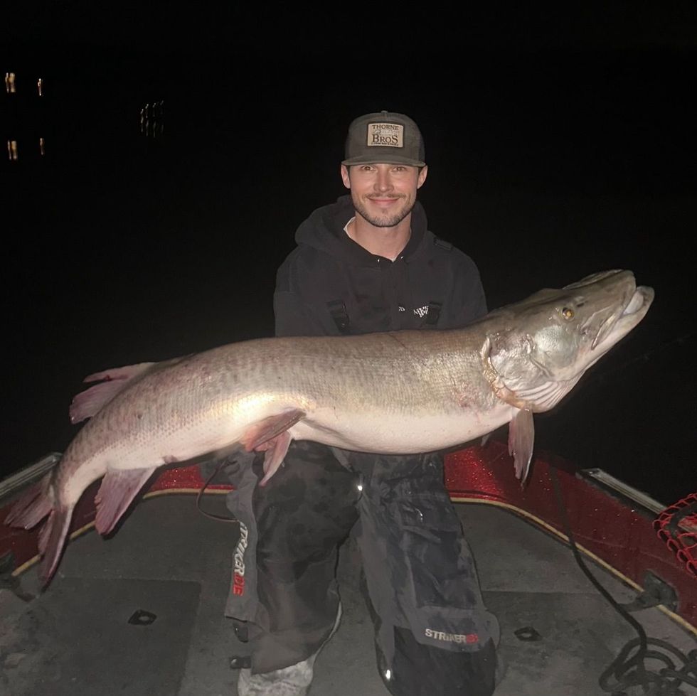 Man on boat holding a large muskellunge fish at night.