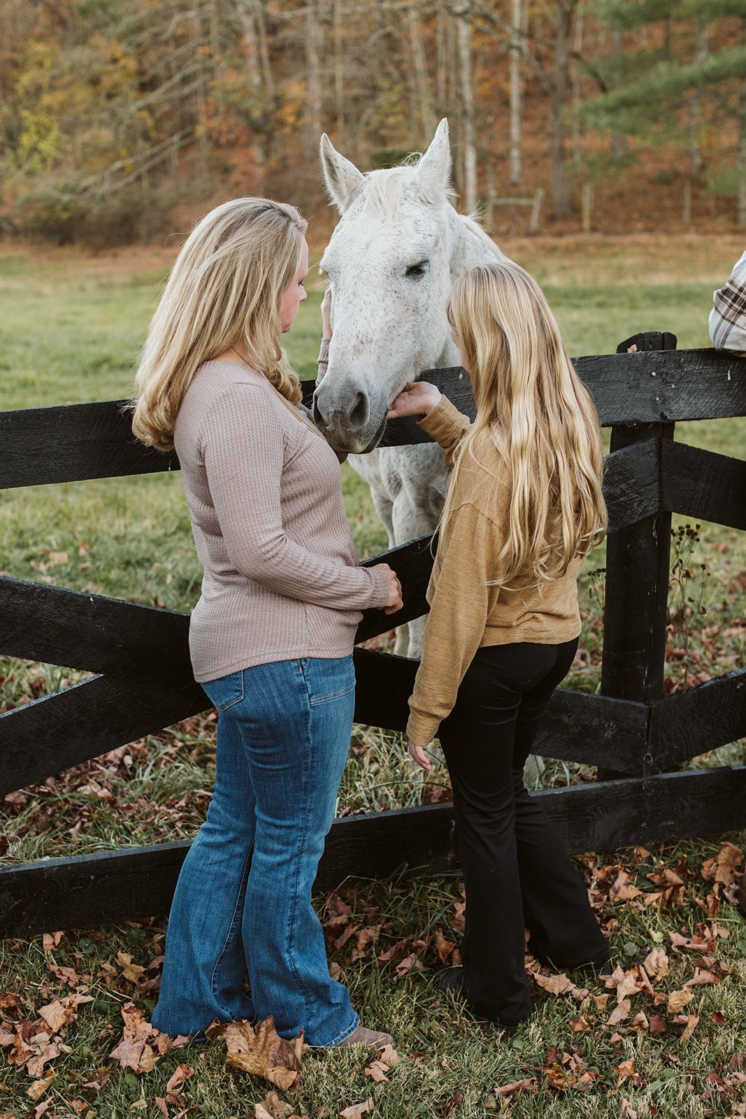 Two women are petting a white horse behind a fence.