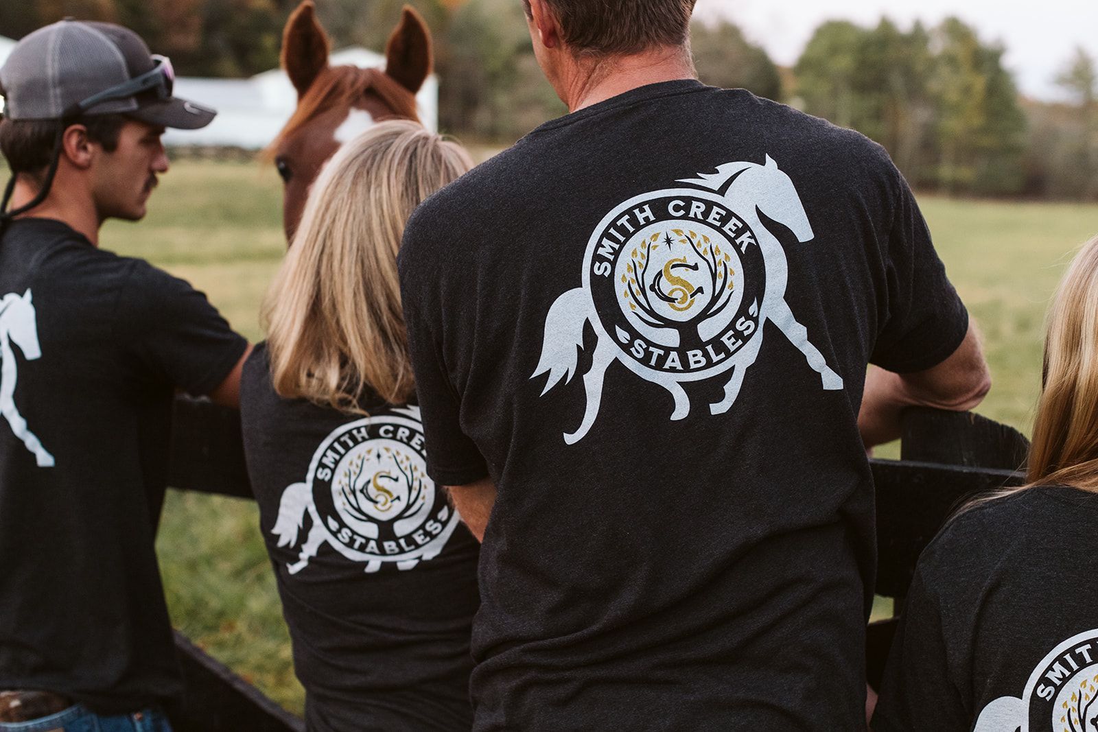 A group of people wearing black shirts with horses on them are standing in front of a horse.