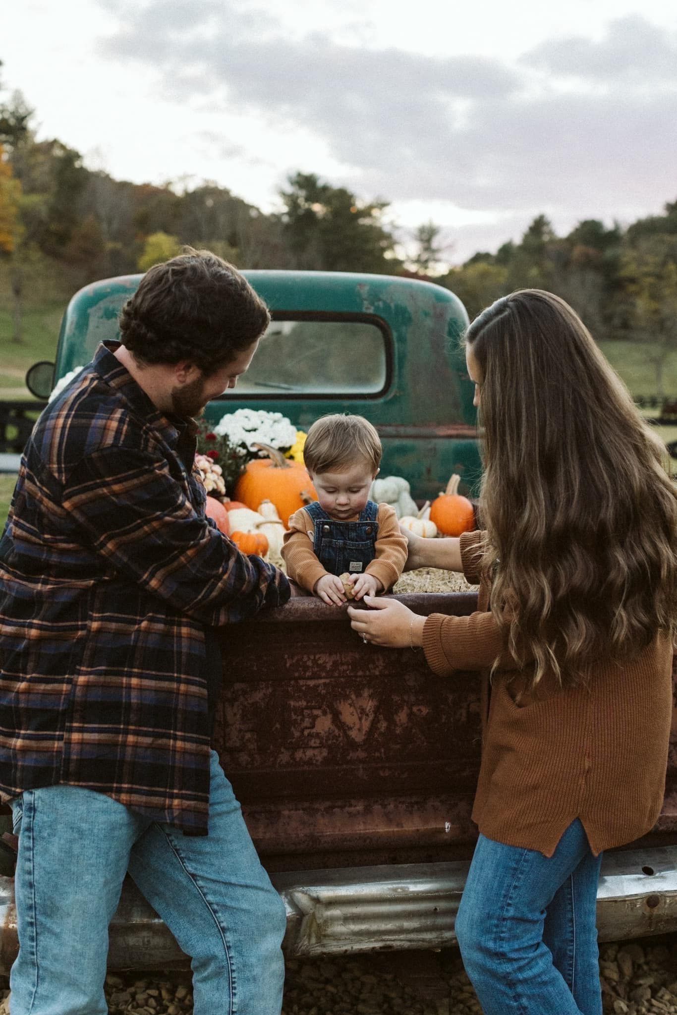 A family is putting pumpkins in the back of a truck.