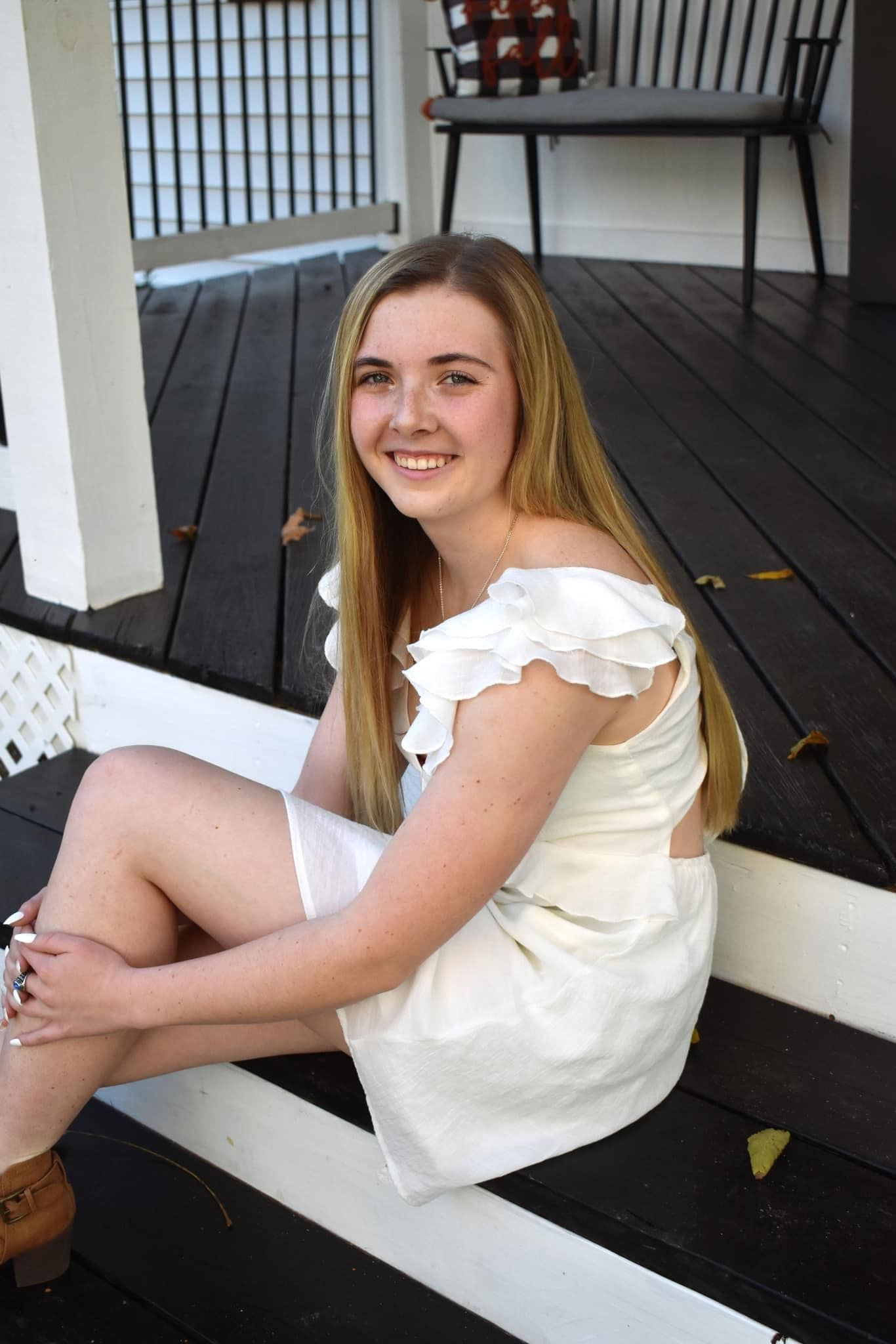 A young woman in a white dress is sitting on a porch.