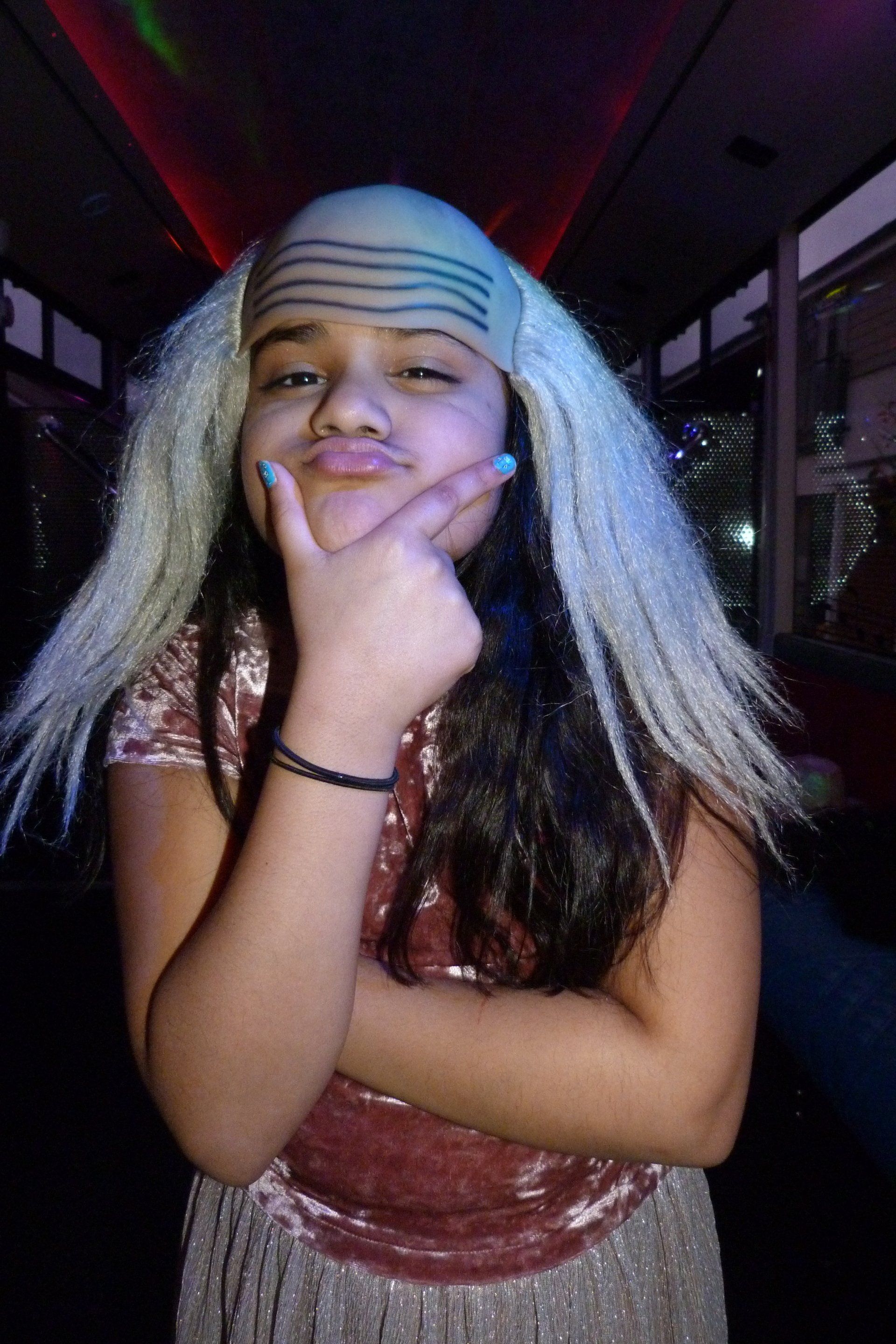 A young girl wearing a wig and a bandana is making a funny face.